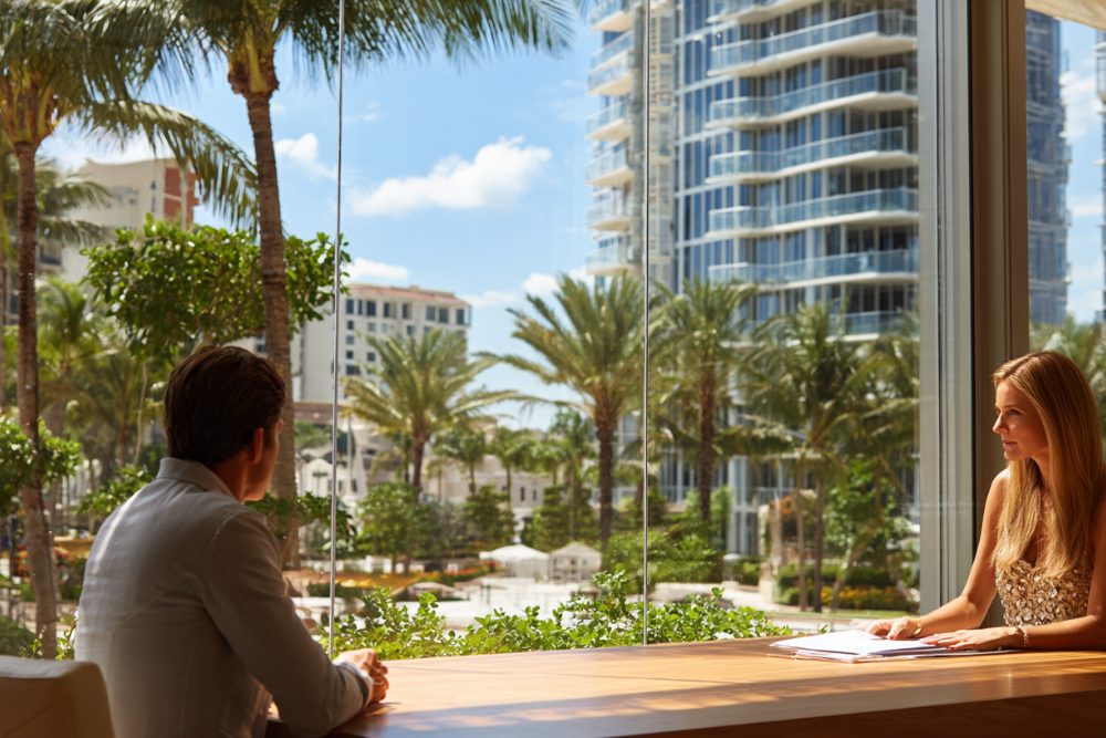 Attorney and client reviewing documents beside a window overlooking Palm Beach County palms and high-rise condominiums during a high net worth divorce