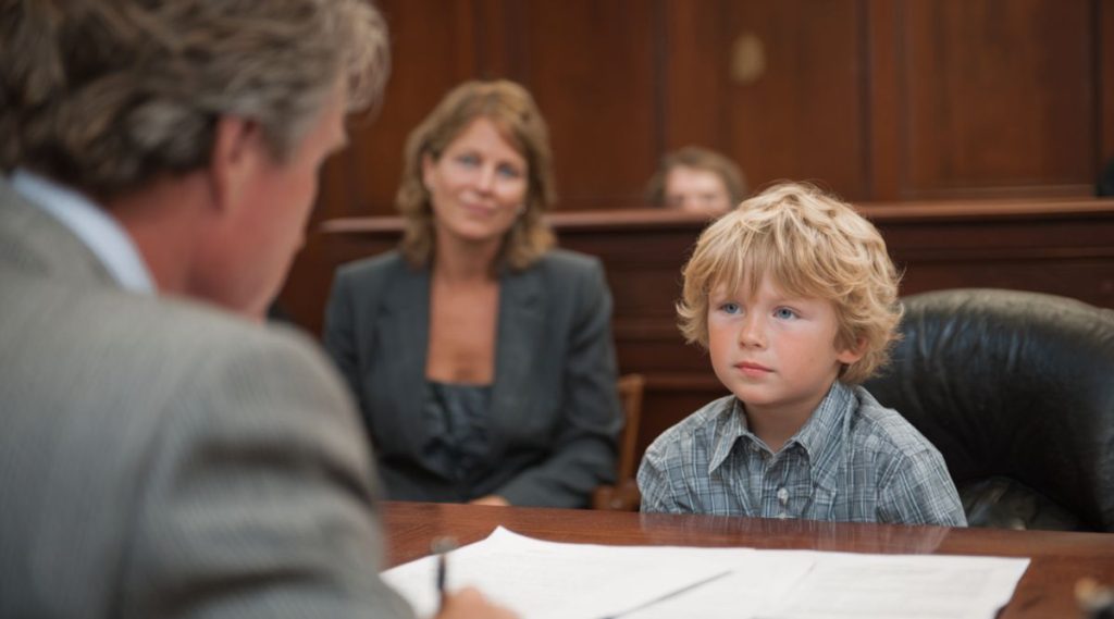 Man at a desk writing while a young boy sits across from him and two women look on, representing modified visitation orders