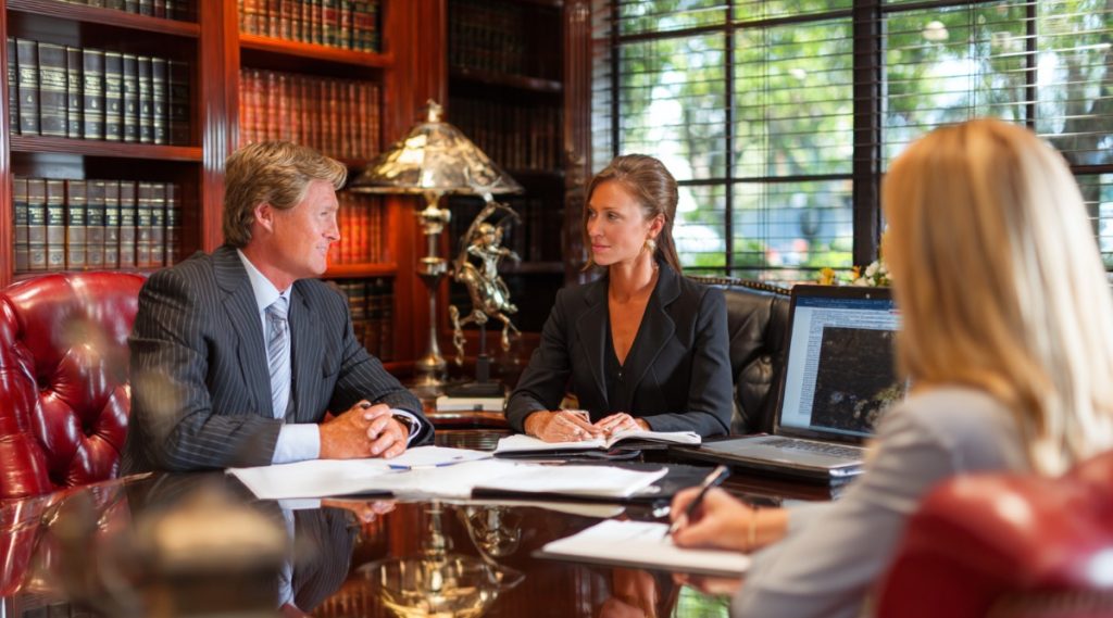 Three people seated at a conference table with paperwork and a laptop, preparing for divorce mediation
