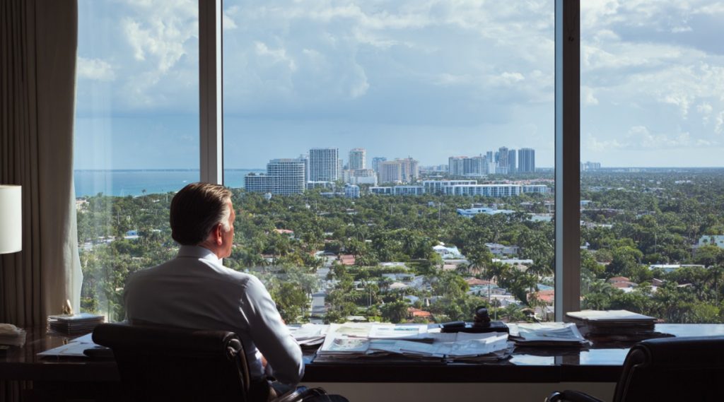 Man seated facing windows over a coastal city skyline, on whether a Florida business can be divided in a Massachusetts divorce