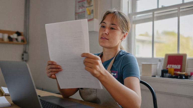 Self-employed New England small-business owner reviewing ledgers and books on a laptop for a child support income analysis