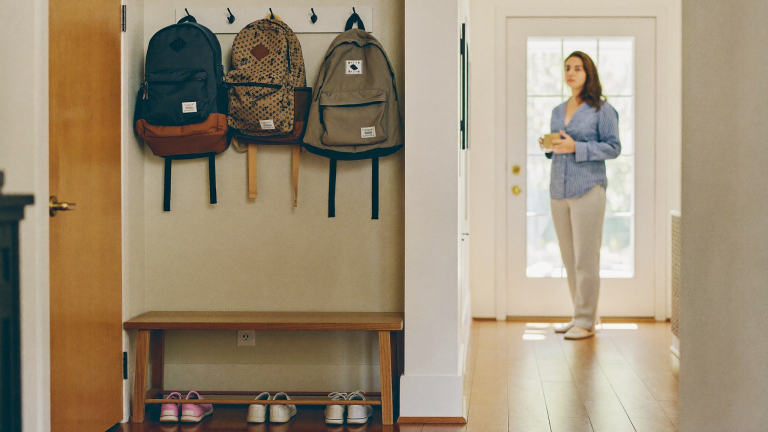Shared-custody family calendar and two children's backpacks by a New England mudroom door in morning light, parenting time and child support